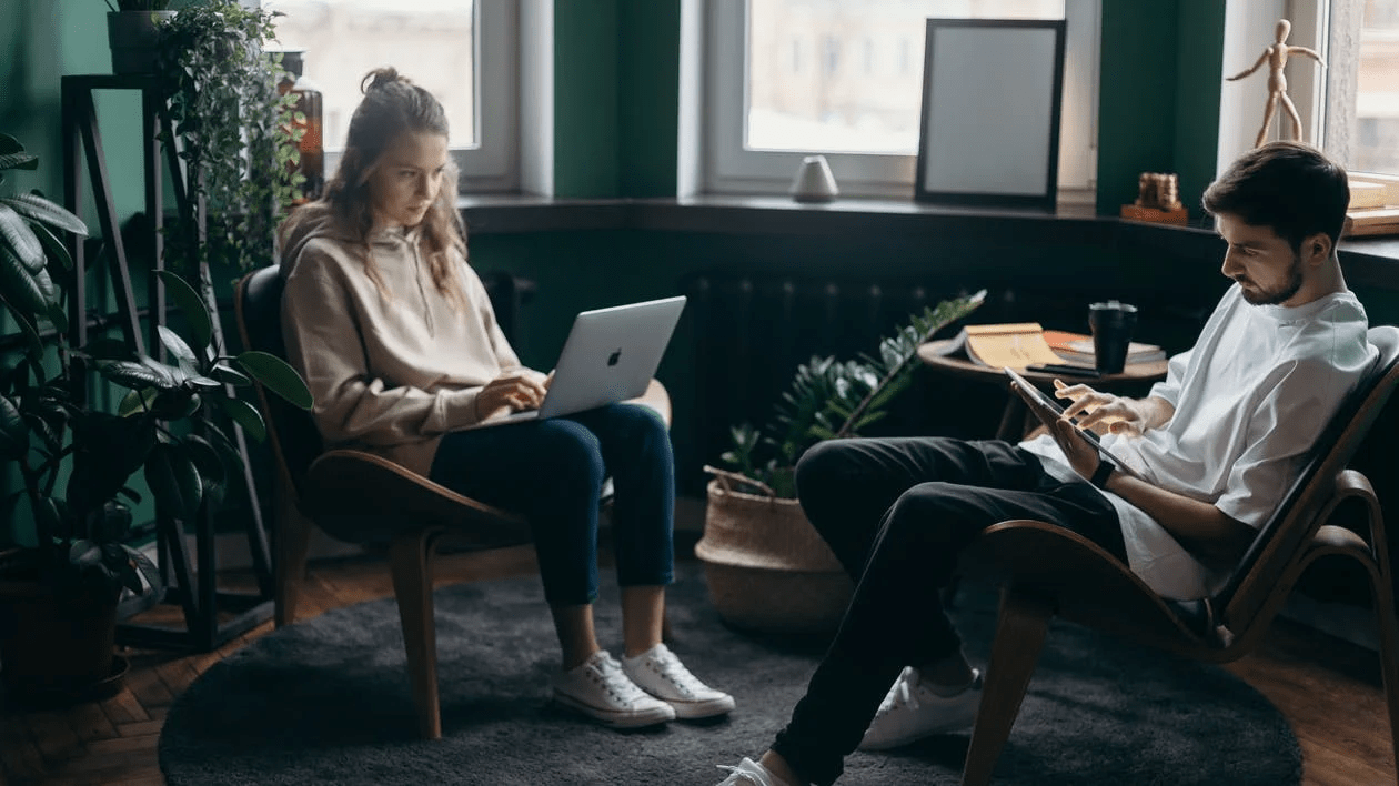 two people sitting together and using a laptop and a tablet